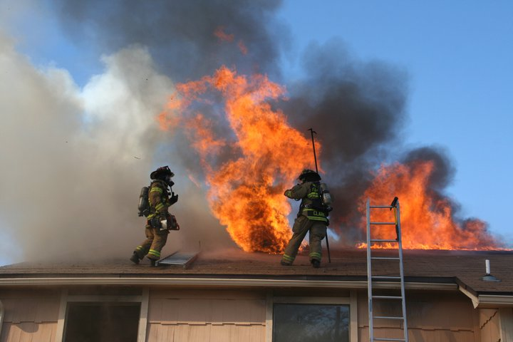 Photo of firefighters on a roof that is on fire