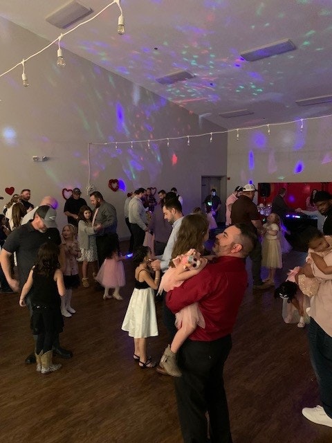 An indoor party with colorful lights, people dancing, and heart decorations on the wall.