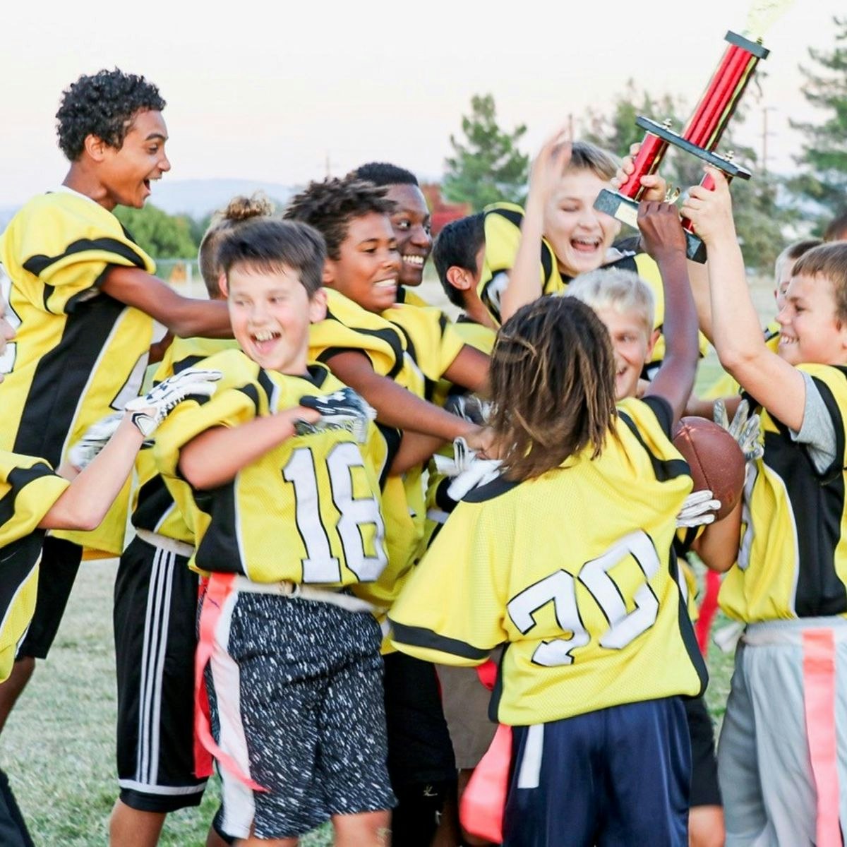 A group of young boys in yellow football uniforms celebrates a victory, holding a trophy and displaying joy and excitement.