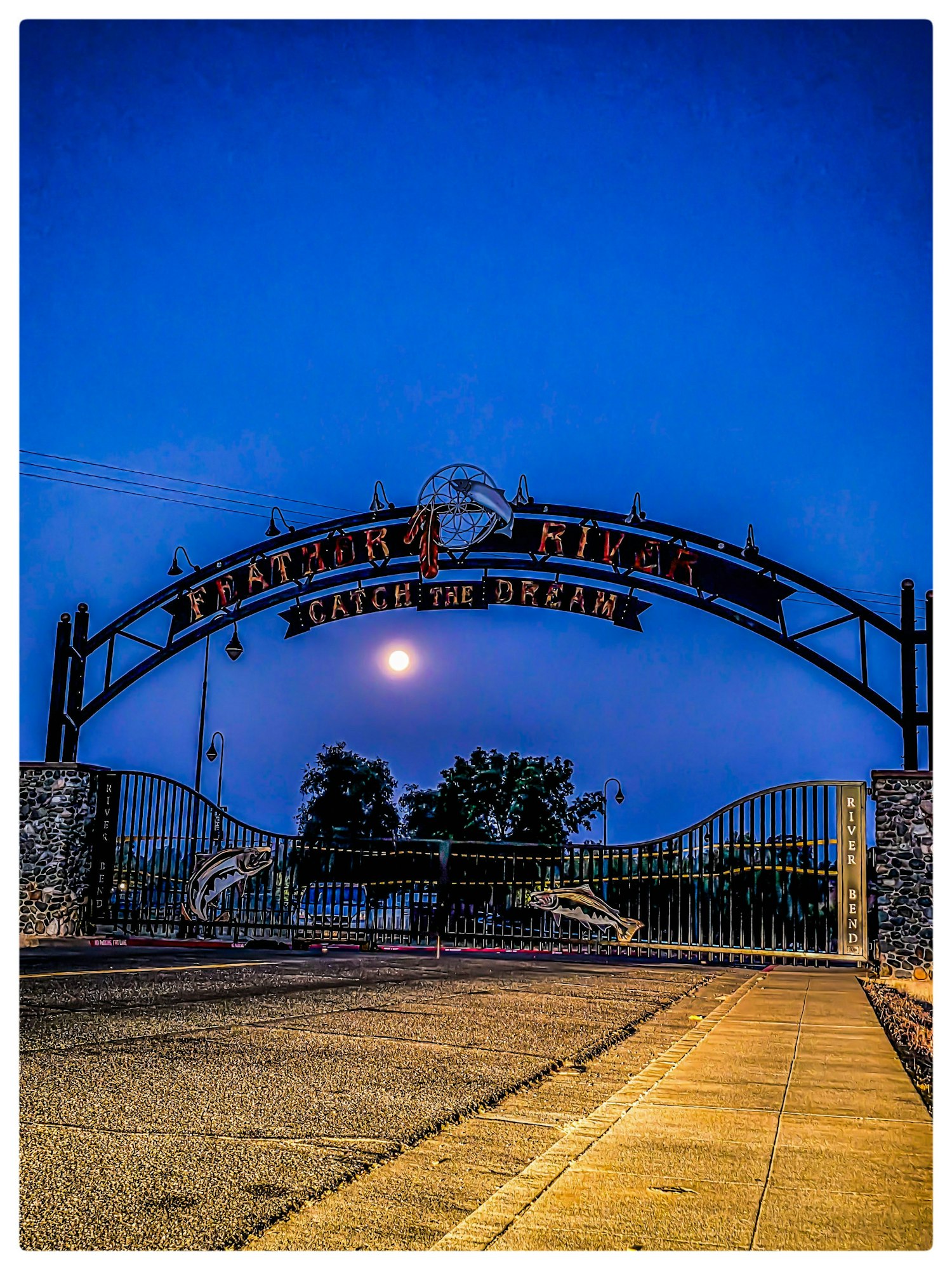 Gate with "Feather River" and "Catch the Dream" signage, moon in the sky, trees in the background.