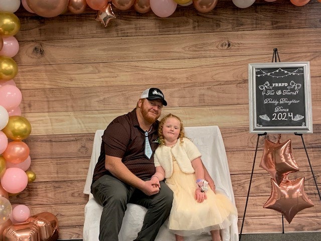 Two people sitting with balloons and a sign, possibly at a celebration or event.