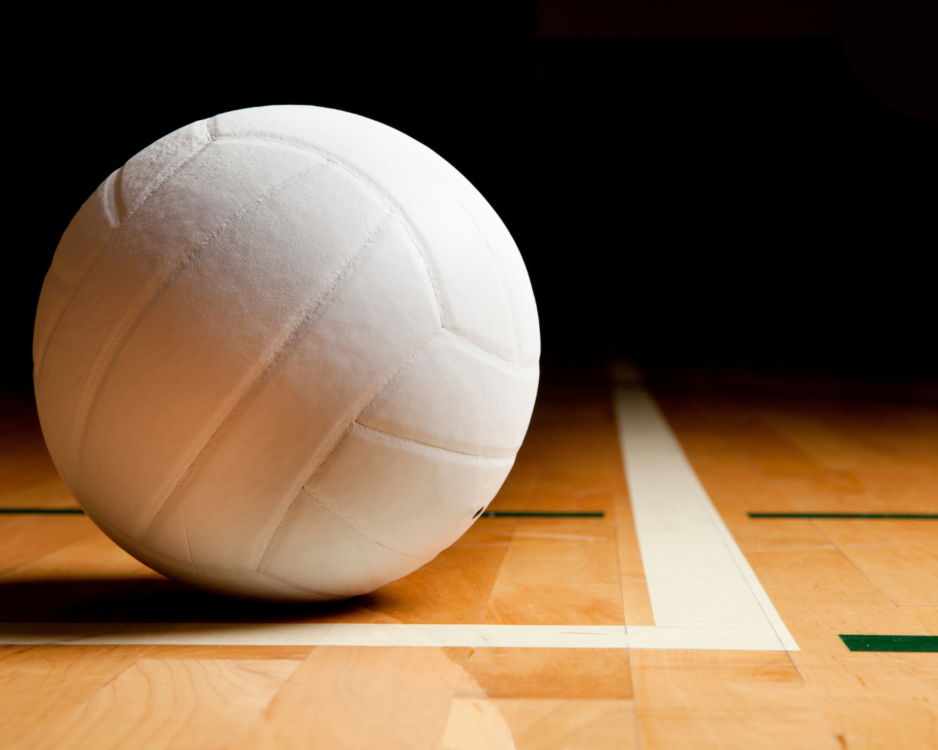 A white volleyball on a wooden gym floor with court lines.