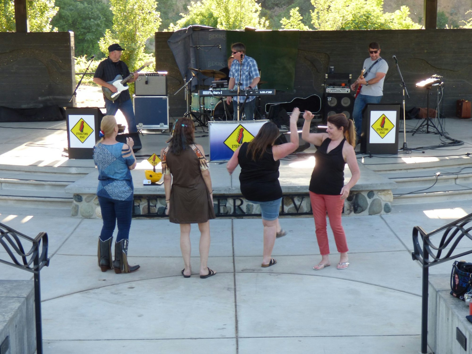 A band plays music on an outdoor stage while four people dance and enjoy the performance.