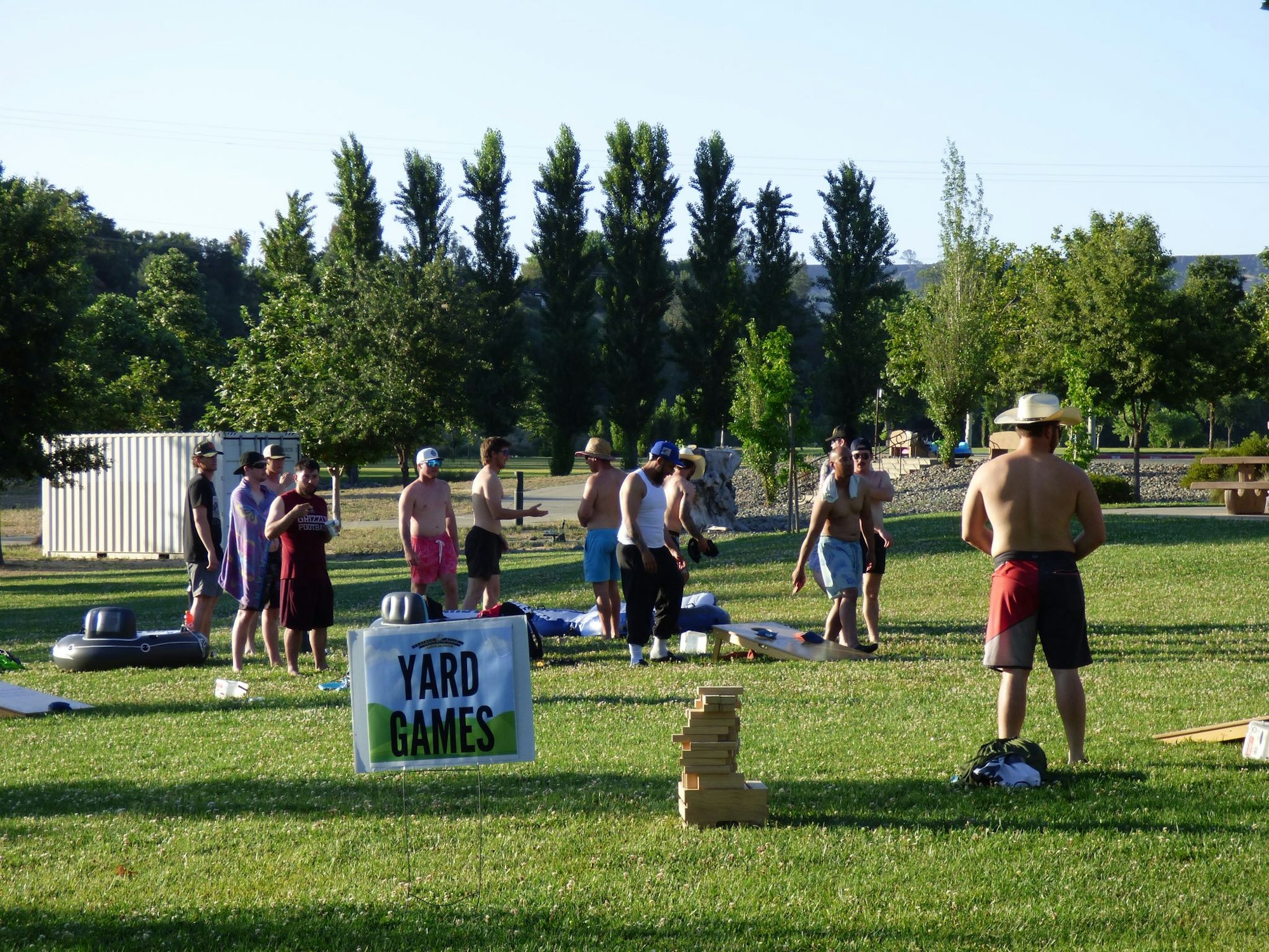 A group of people playing yard games in a park with a "Yard Games" sign visible.