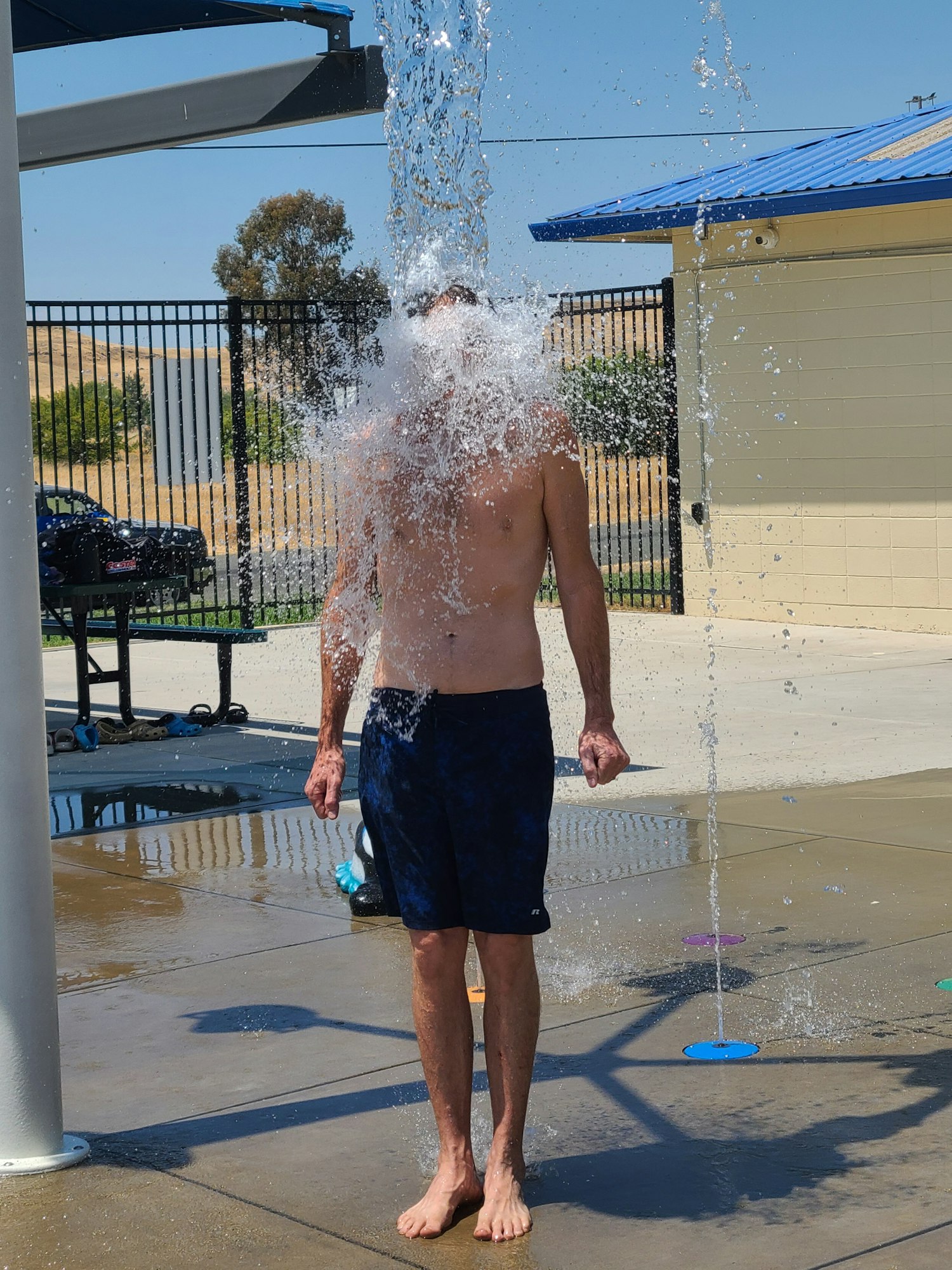 Person standing under a stream of water at a splash pad, with water splashing onto their head.