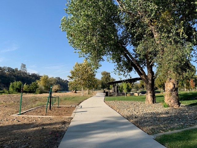 A paved path in a park with trees, exercise equipment on the side, and a hill in the background.