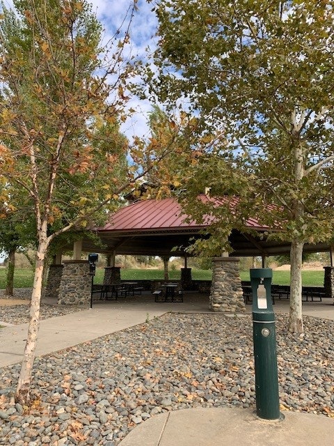 Park pavilion with picnic tables, stone pillars, autumn trees, and a drinking fountain.