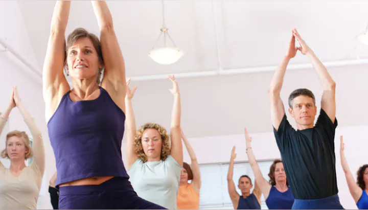 A group of individuals practicing yoga in a well-lit studio, focusing on poses with arms raised.