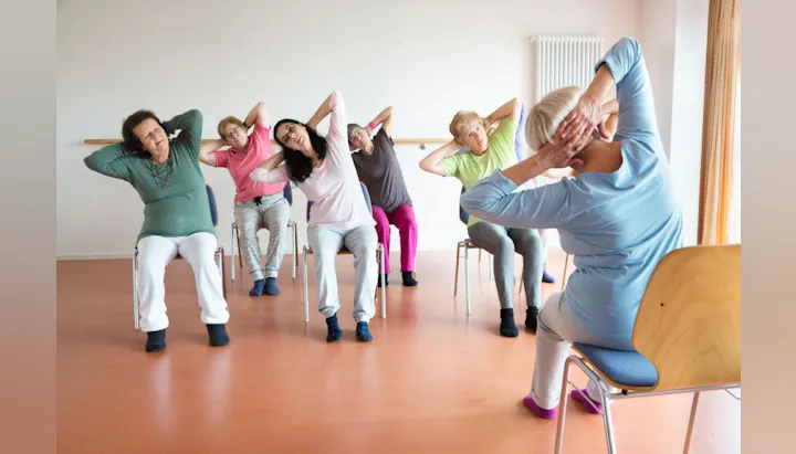 A group of elderly women participating in a seated exercise class, stretching and promoting physical wellness.