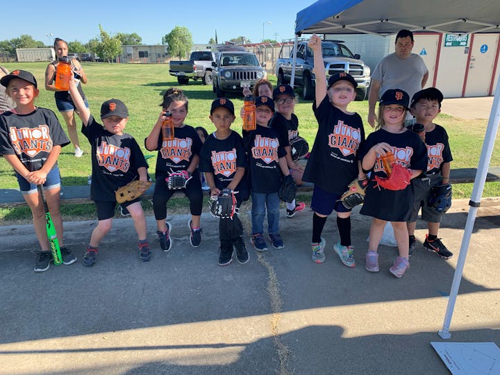 A group of kids wearing "Junior Giants" shirts have fun at a baseball event, showcasing their gear and excitement.