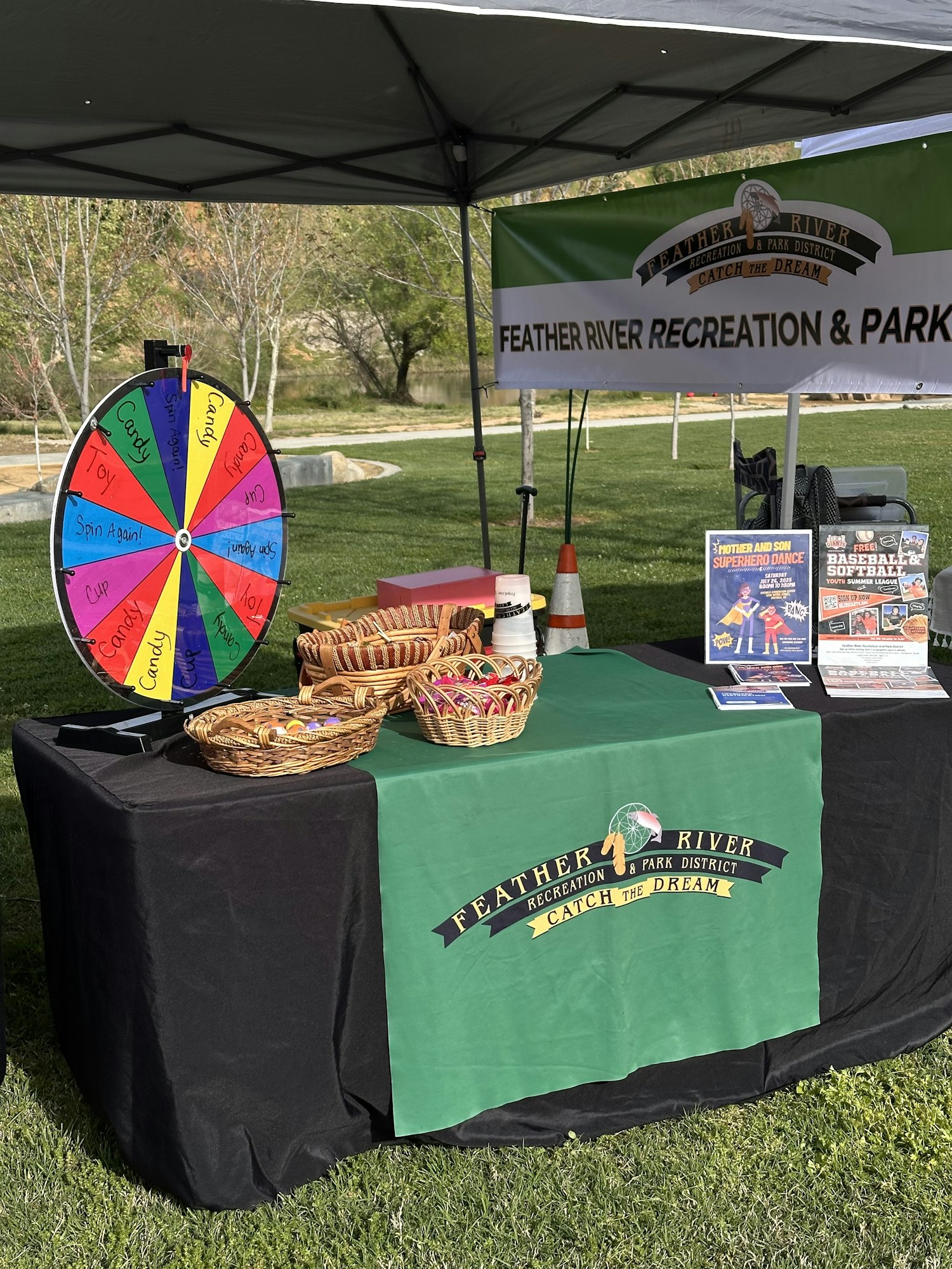 Outdoor booth with a prize wheel, baskets of candy, and promotional materials for Feather River Recreation & Park District.