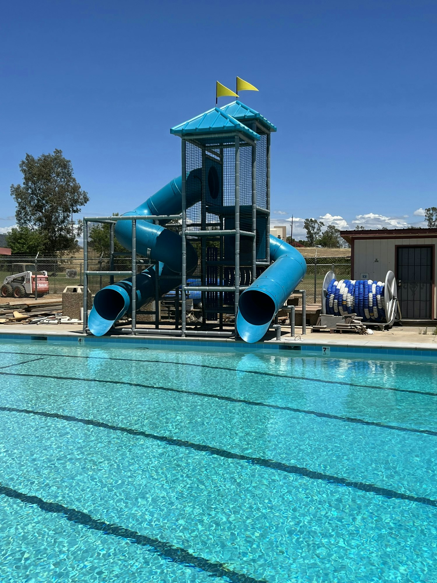 A swimming pool with blue slides and a tower, under a clear blue sky.