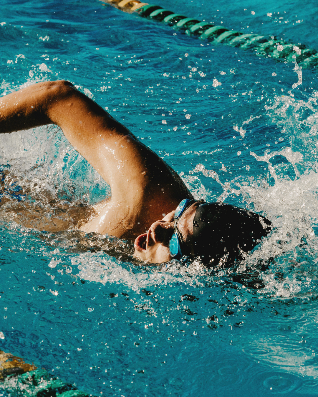 A swimmer wearing goggles and a swim cap is performing the freestyle stroke in a pool.