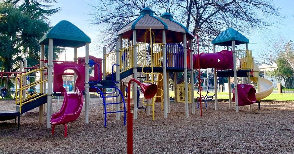 A colorful playground featuring slides, climbing structures, and play equipment set in a grassy park.