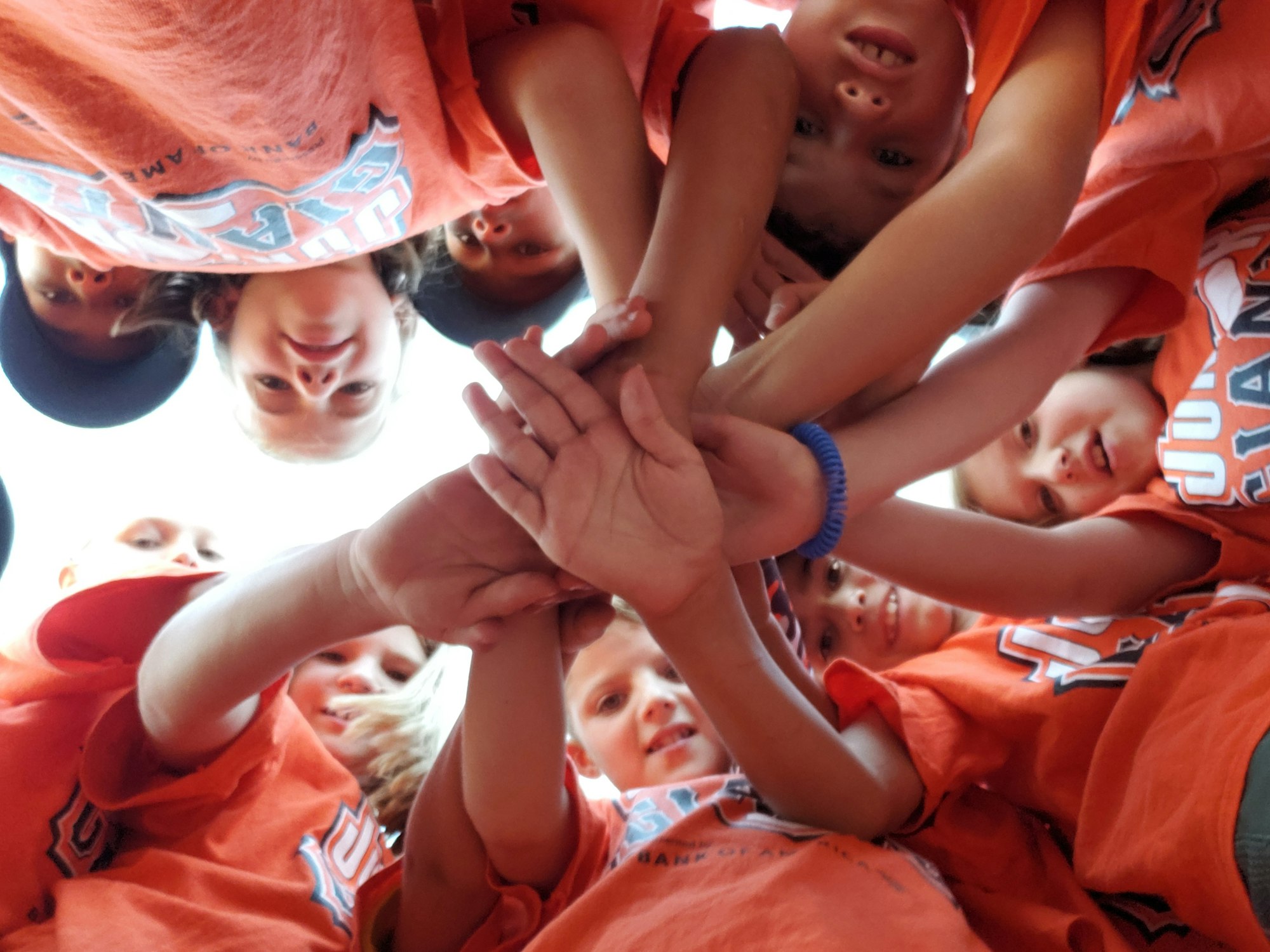 A group of people in orange shirts, joining hands in a circle from a low angle.