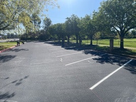 An empty parking lot with trees and a person in the distance.