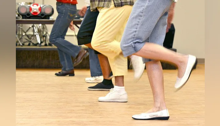 People participating in a dance class, showcasing their legs and shoes as they perform synchronized movements.