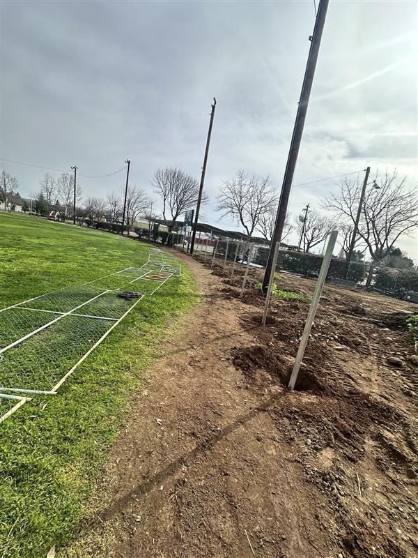 A tilted view of a sports field with goalposts and fencing under construction, on a cloudy day.