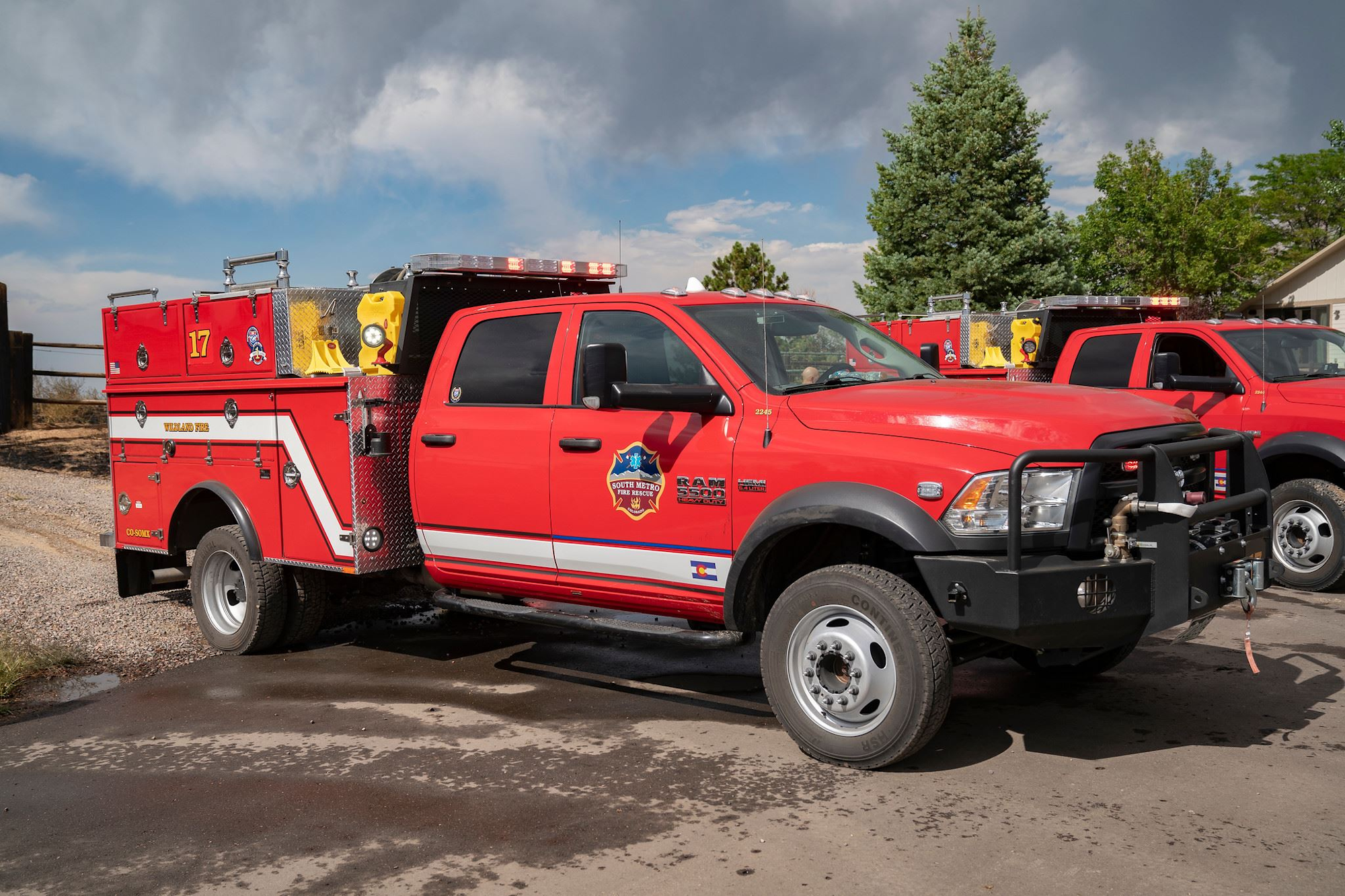 A red fire response vehicle with "WILDLAND FIRE" and a logo, parked on a sunlit street.