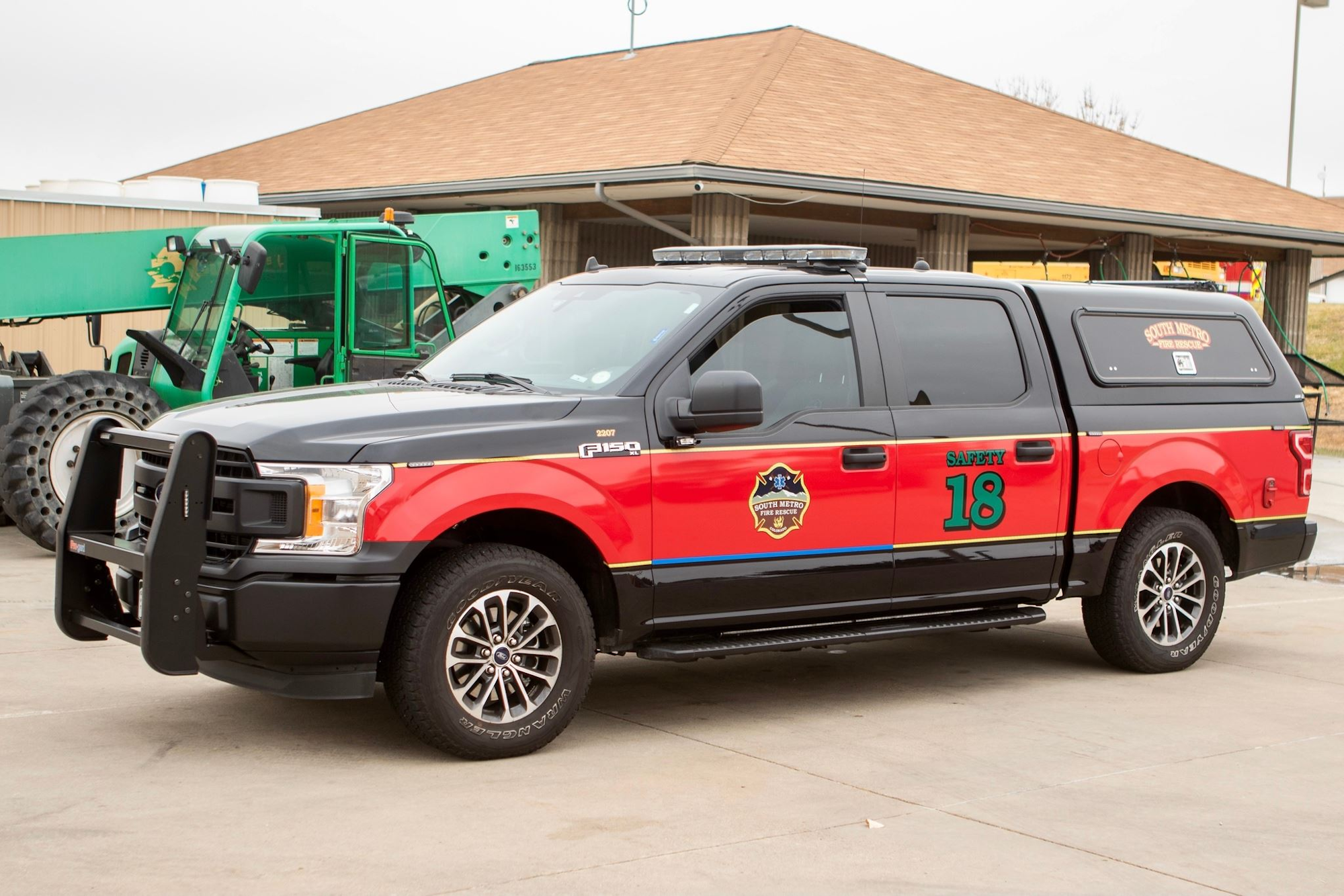 Red and black fire department truck labeled "Safety 18" parked next to green equipment.