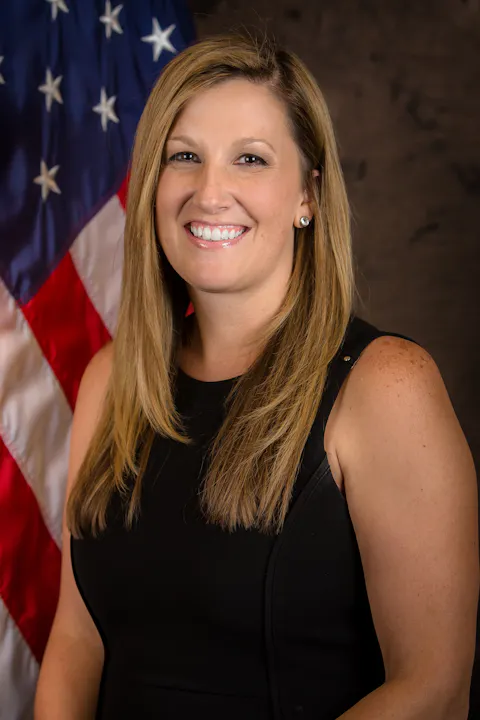 A woman smiling, standing in front of the American flag.