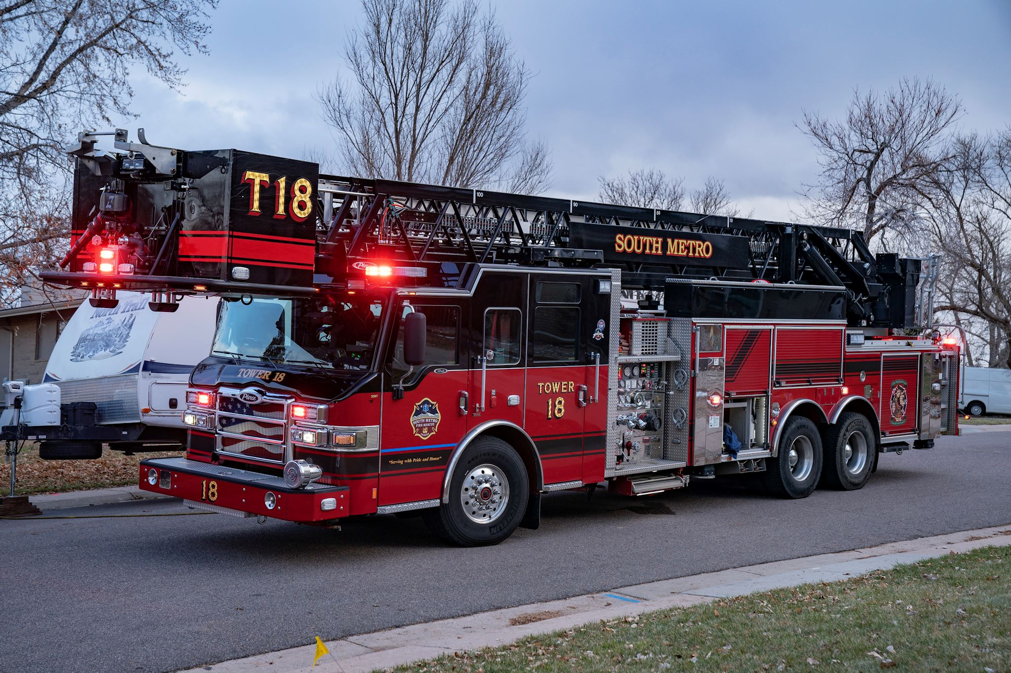 A red fire truck labeled "Tower 18" from South Metro, featuring a ladder and emergency lights, parked on a street.