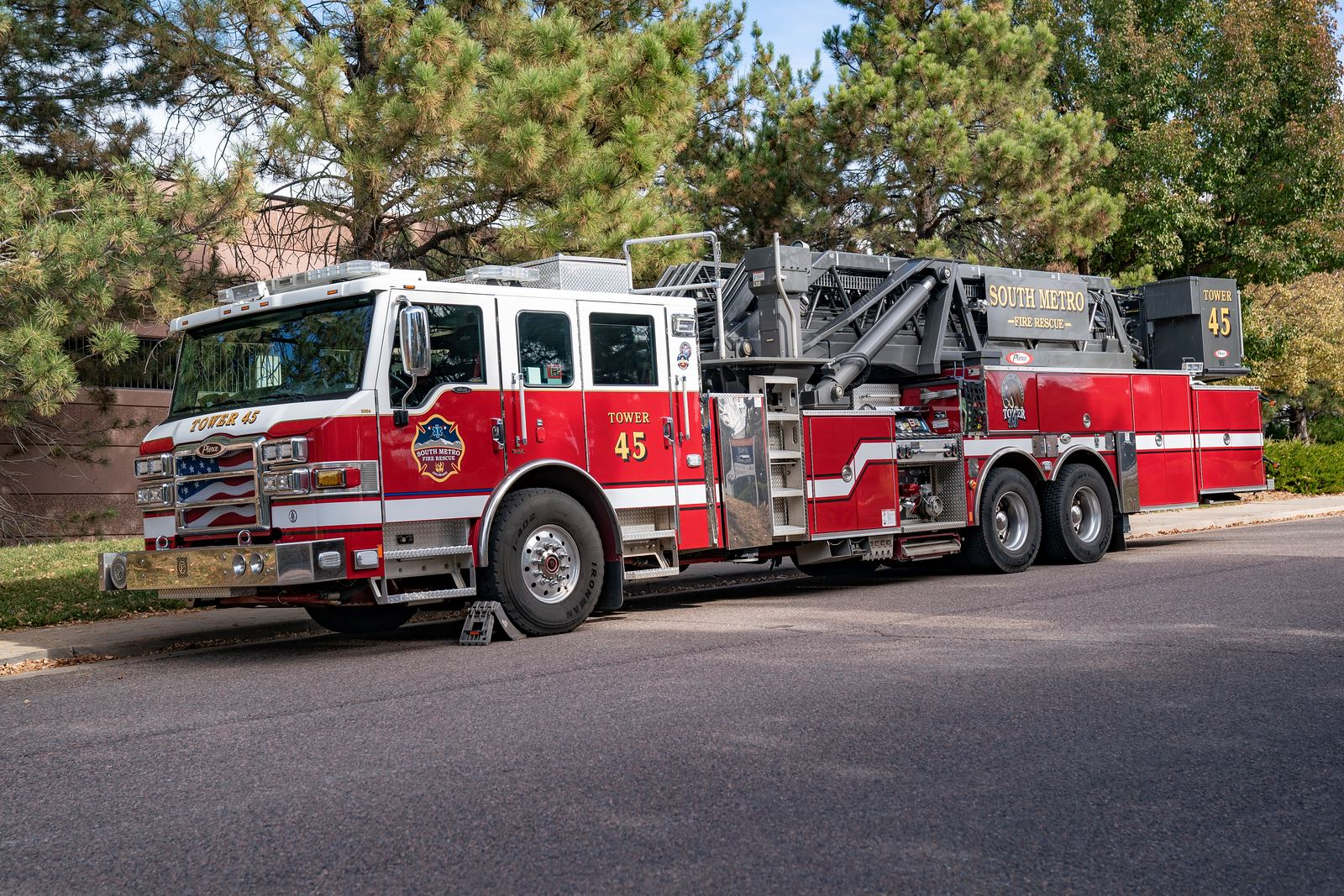 A red fire truck labeled "Tower 45" parked on a street beside a tree-lined area.