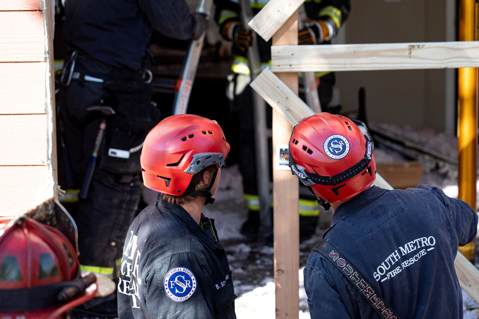 Rescue workers in red helmets and gear at a structural site, preparing for an operation.