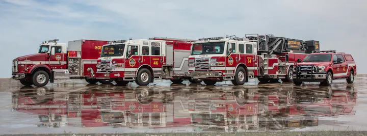 A lineup of fire trucks and a fire department SUV with reflections on a wet surface.