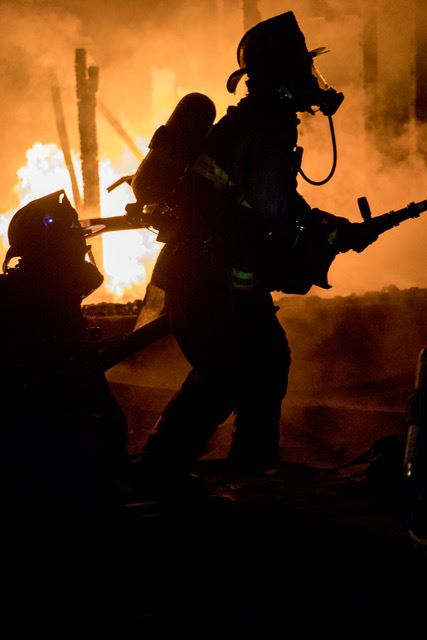 Firefighters battling a blaze, with flames in the background.