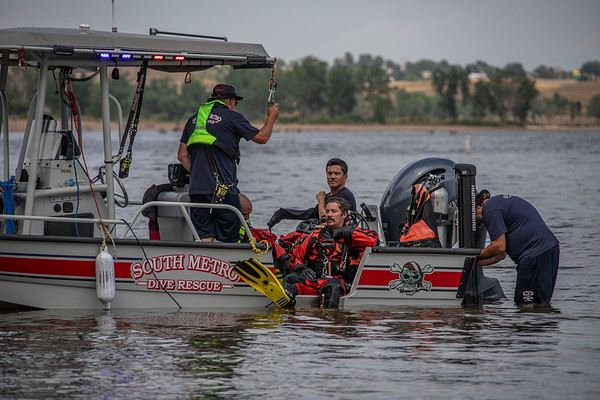 Rescue team on a boat labeled "South Metro Dive Rescue" with a diver in gear, preparing for a water operation.
