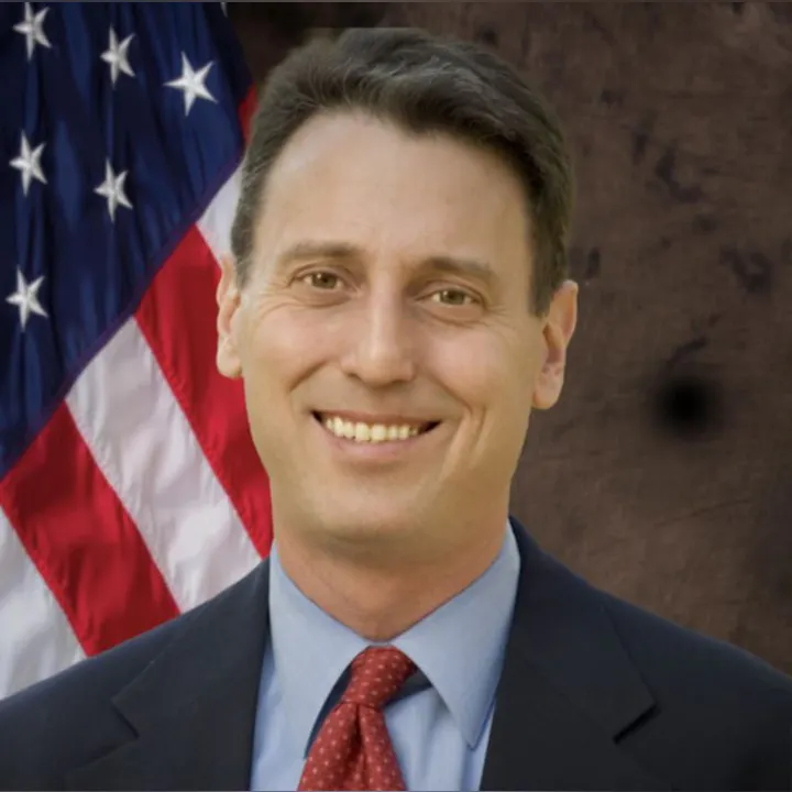 A person smiling in front of an American flag.