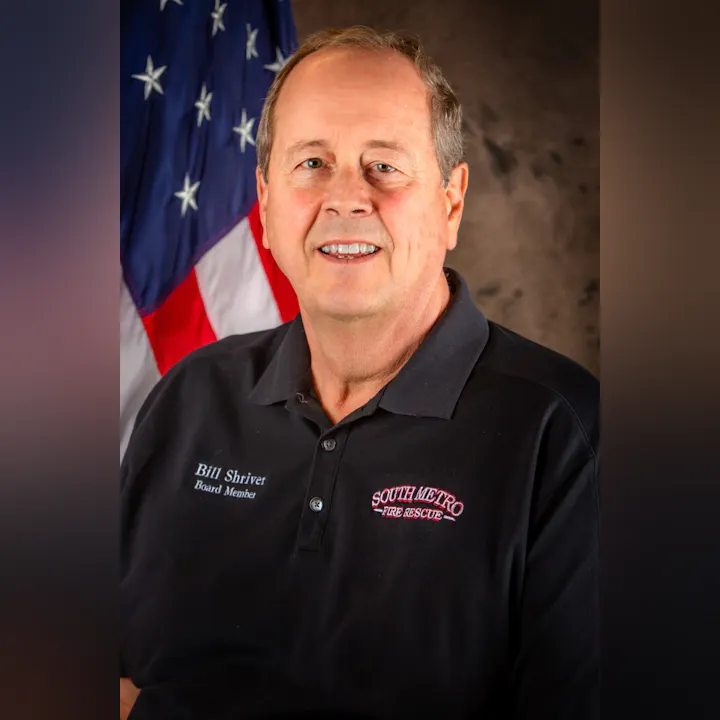 A person wearing a South Metro Fire Rescue polo with "Board Member" text, posing in front of a U.S. flag.