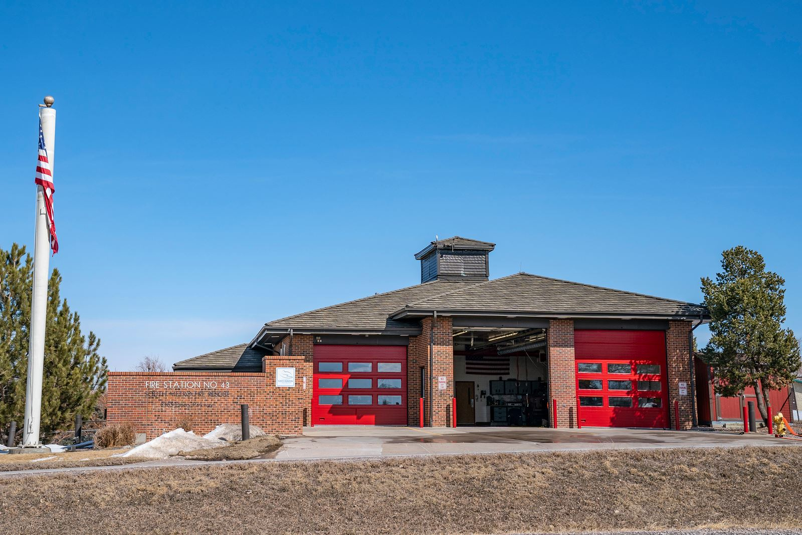 A fire station with red doors, an American flag on a pole, and a clear blue sky.
