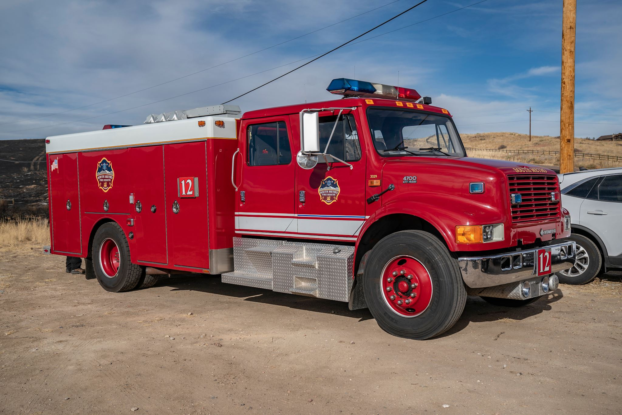 A red fire truck labeled "12" parked on a dirt road under a clear blue sky.