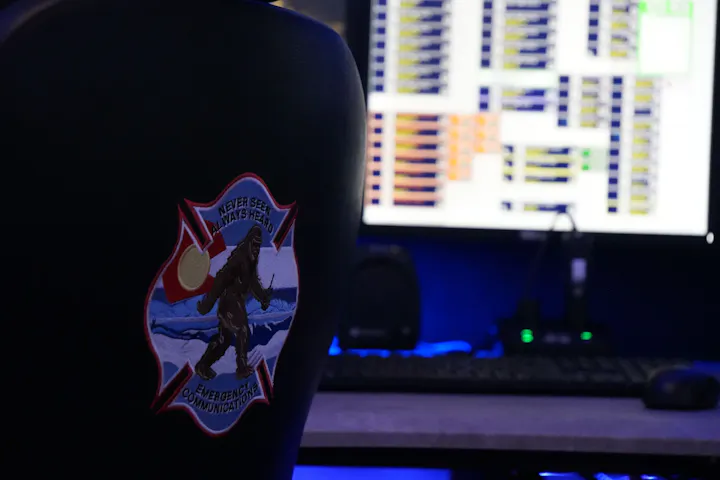 An office setting featuring a chair with a patch depicting a Bigfoot-like creature and a screen displaying data or charts.