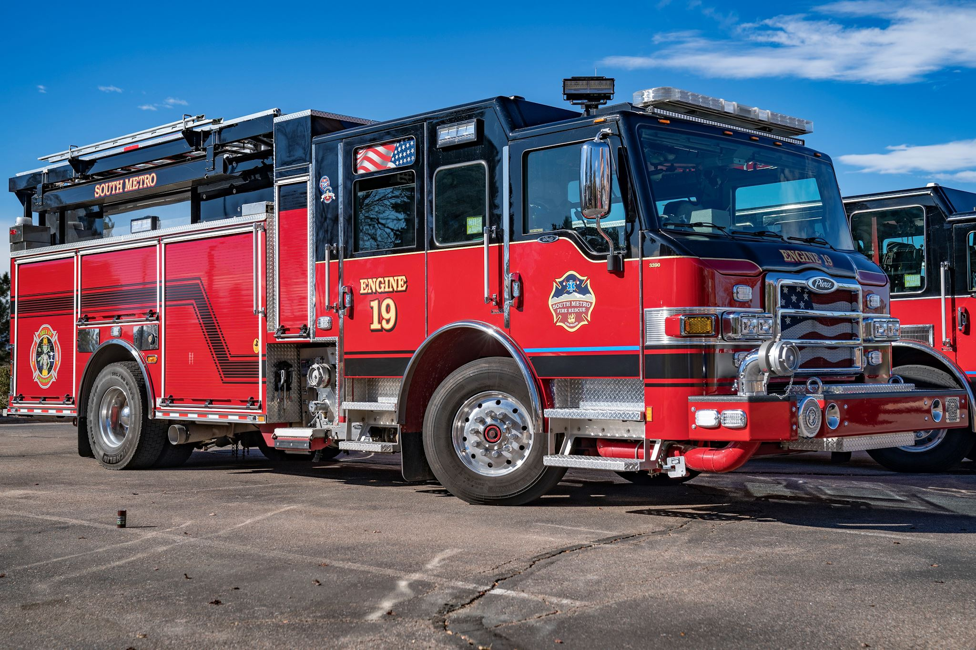 A red fire truck labeled "Engine 19" from the South Metro fire department parked on pavement under a clear blue sky.