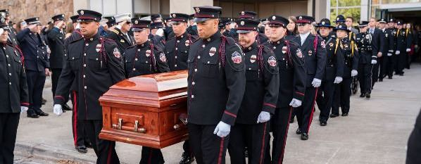 Uniformed personnel carry a wooden casket in a formal procession.