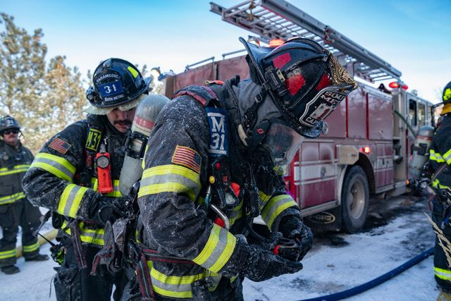 Firefighters in full gear alongside a fire truck on a snowy day.