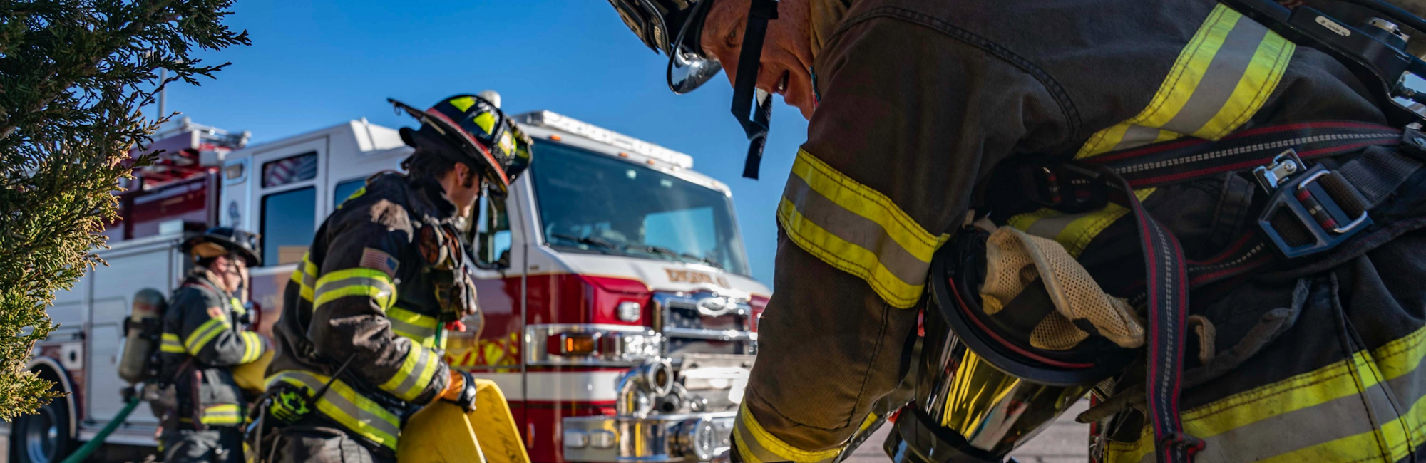 Firefighters in gear, with a fire truck in the background, preparing equipment.