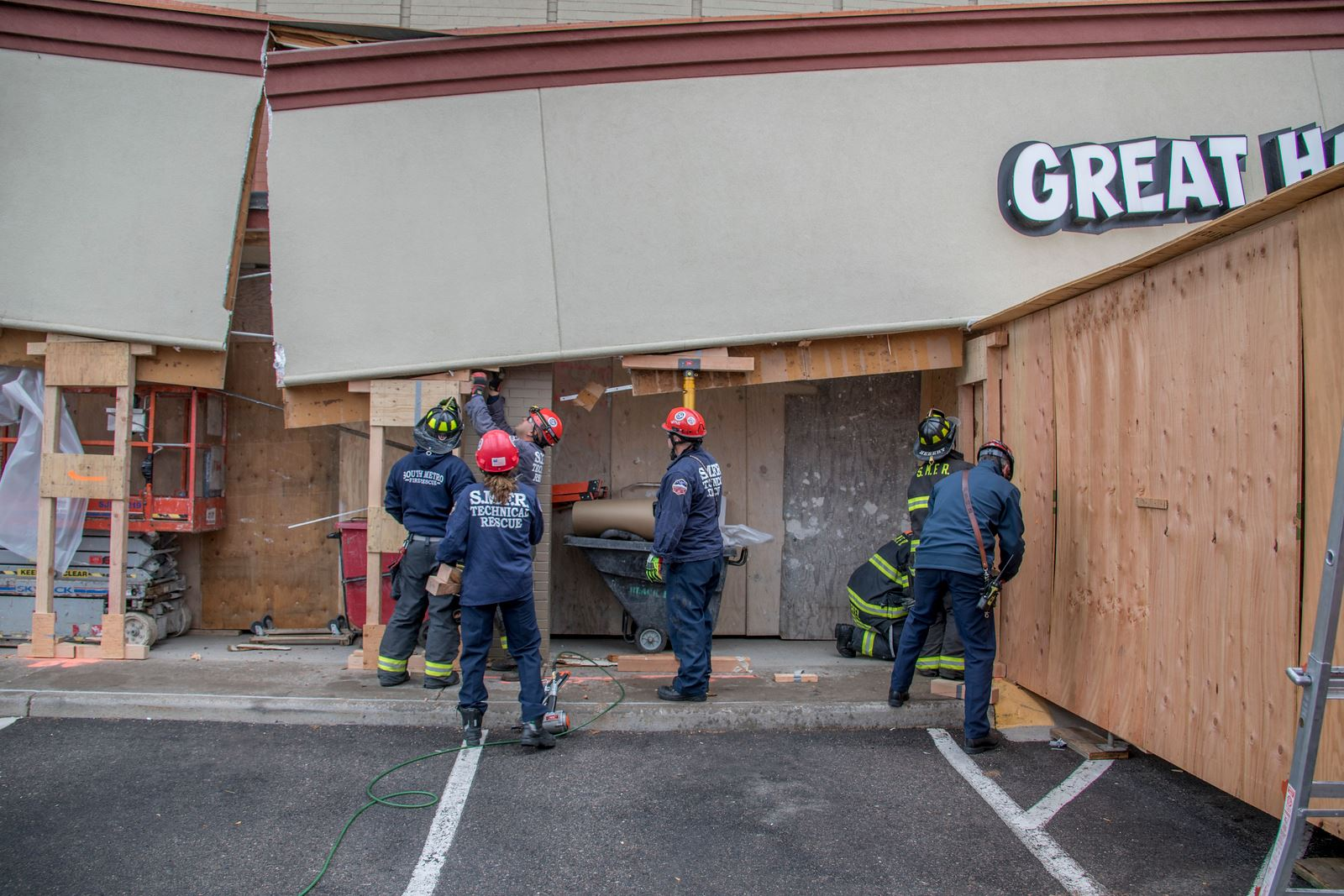 Firefighters assessing a partially collapsed building facade with support beams and equipment.