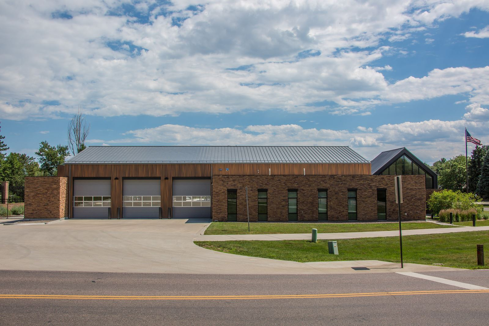 A modern fire station with large garage doors, a brick exterior, and an American flag flying.