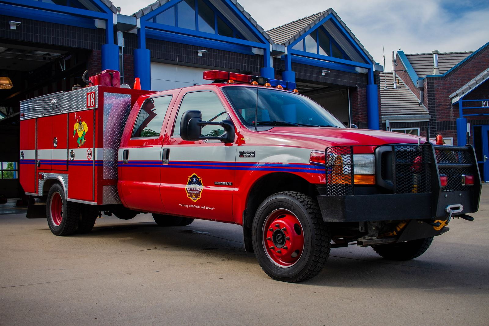 A red fire truck parked in front of a fire station with blue accents and garage doors.