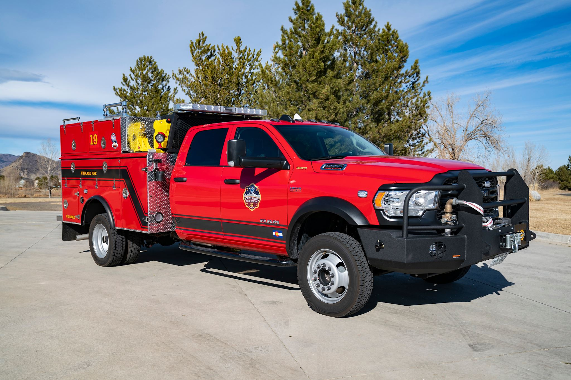 A red fire rescue truck parked on a concrete surface, surrounded by trees under a blue sky.