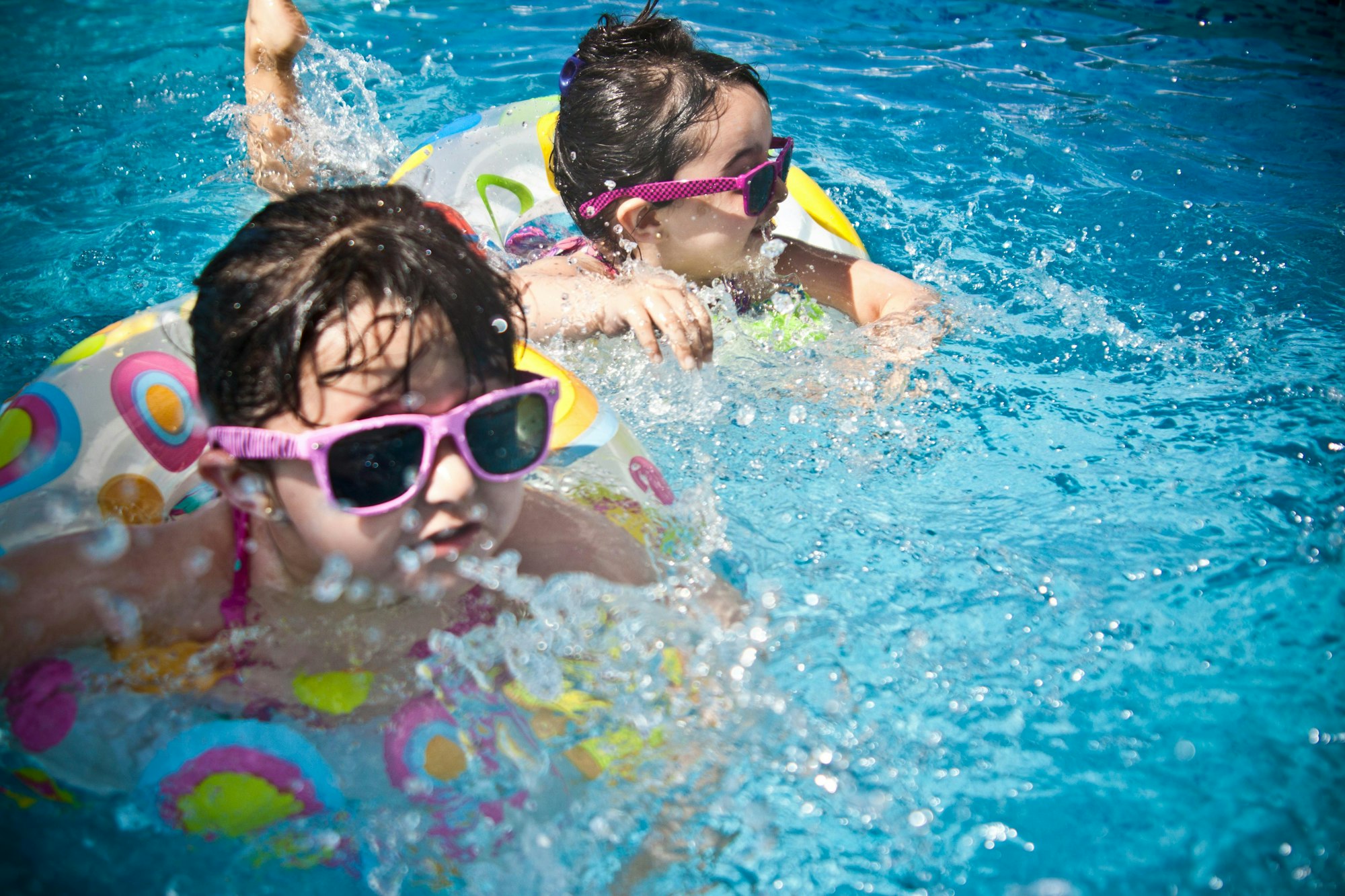 Kids with sunglasses playing in a pool using inflatable rings.