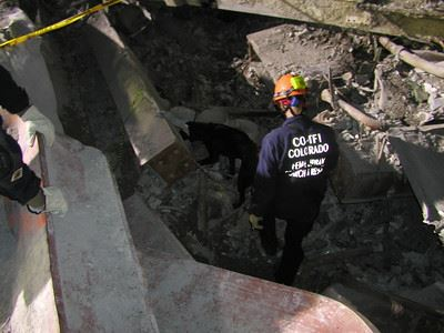 A rescue worker with "CO-TF1 Colorado" on their shirt and helmet navigates through rubble and debris.