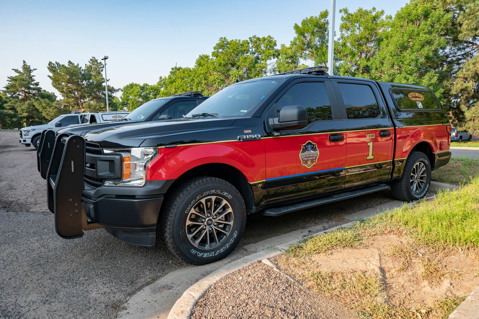 A red and black fire department truck parked near trees, marked "F150" with a shield logo and "MED 1" on the side.