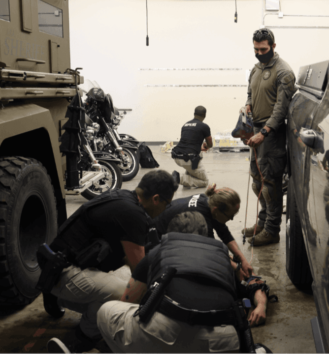 Police officers engage in a tactical training exercise in a garage with motorcycles.