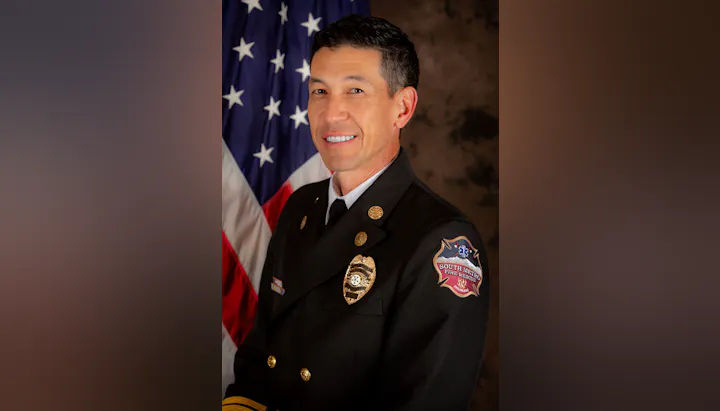 A person in a South Metro Fire Rescue uniform stands in front of a U.S. flag.