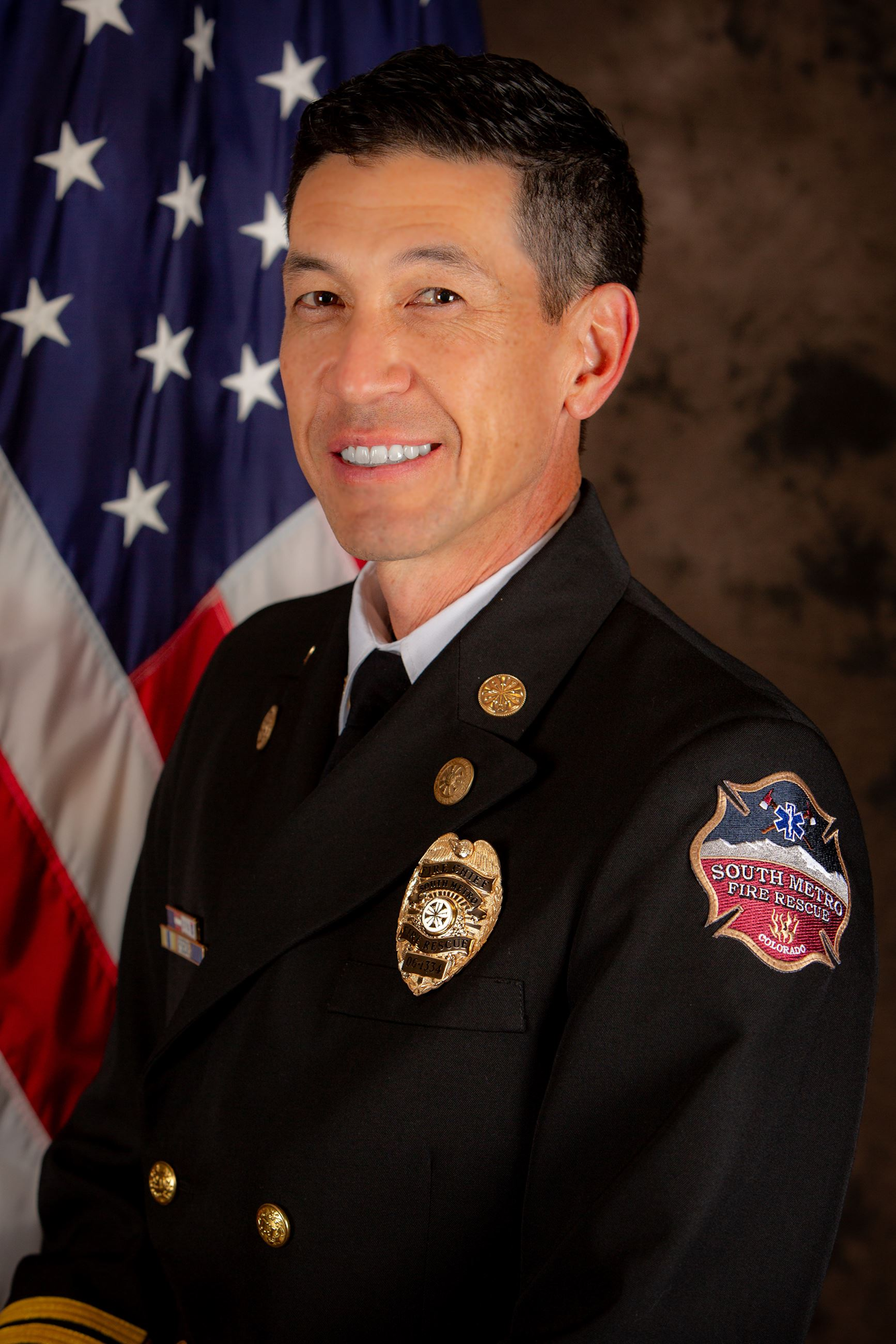 A person in a South Metro Fire Rescue uniform stands in front of a U.S. flag.